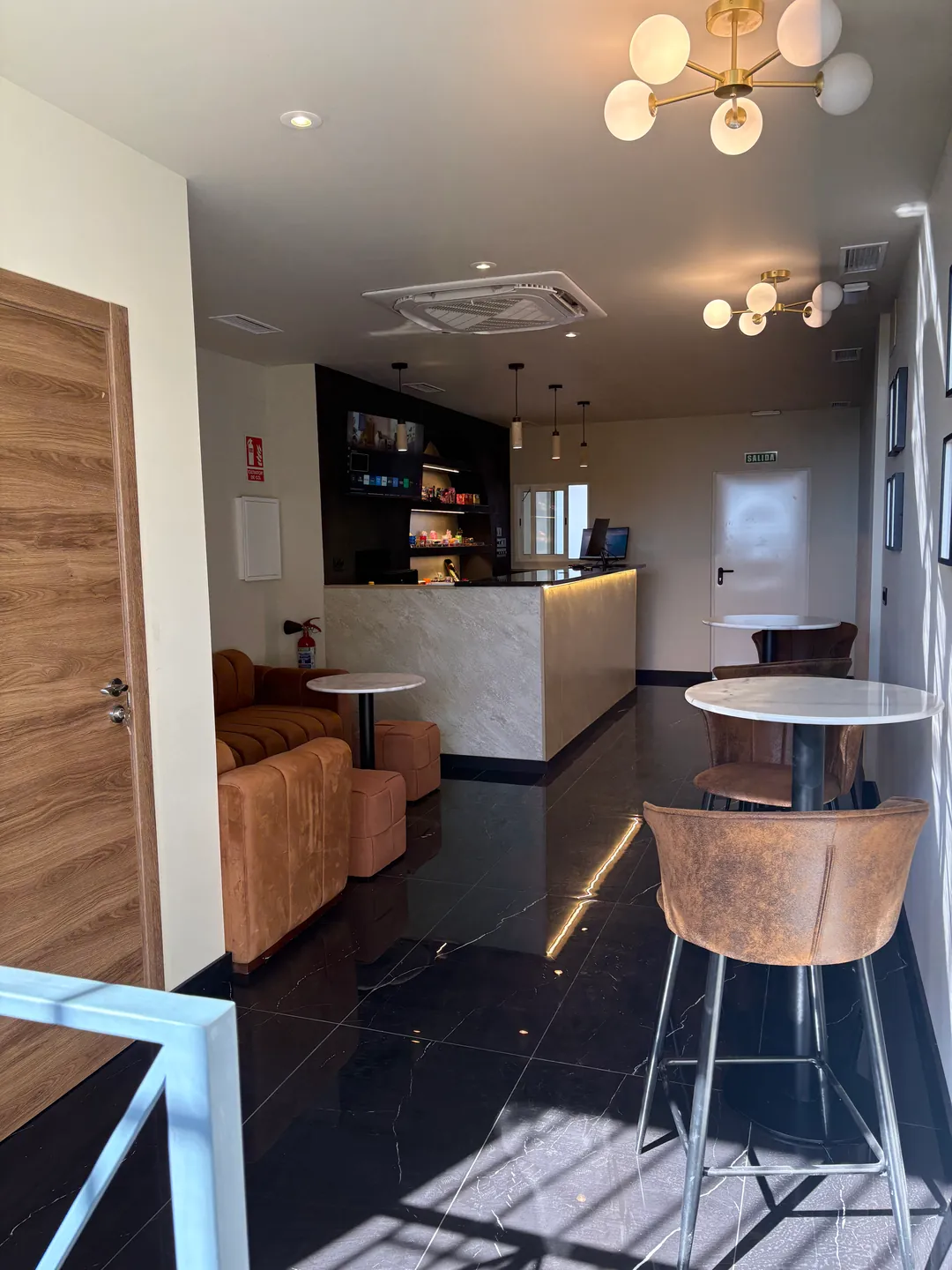 La sala luminosa desde la entrada: lámparas doradas, sillones y la recepción al fondo